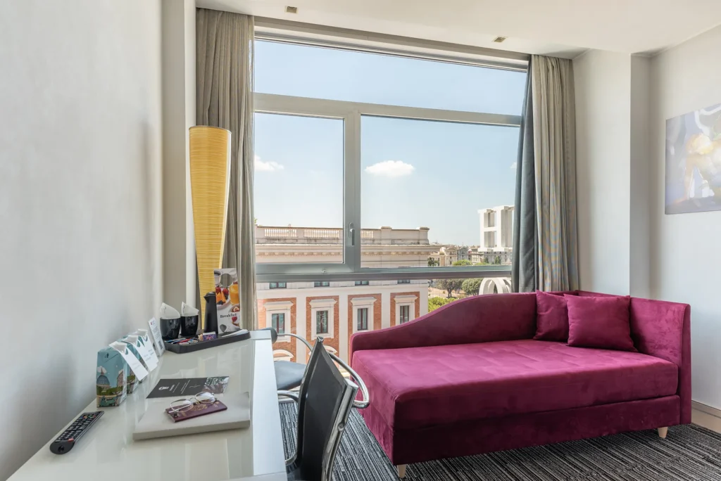 Nell'immagine un angolo relax della camera Deluxe: c'è un divanetto e una scrivania con vista sulla città di Roma.