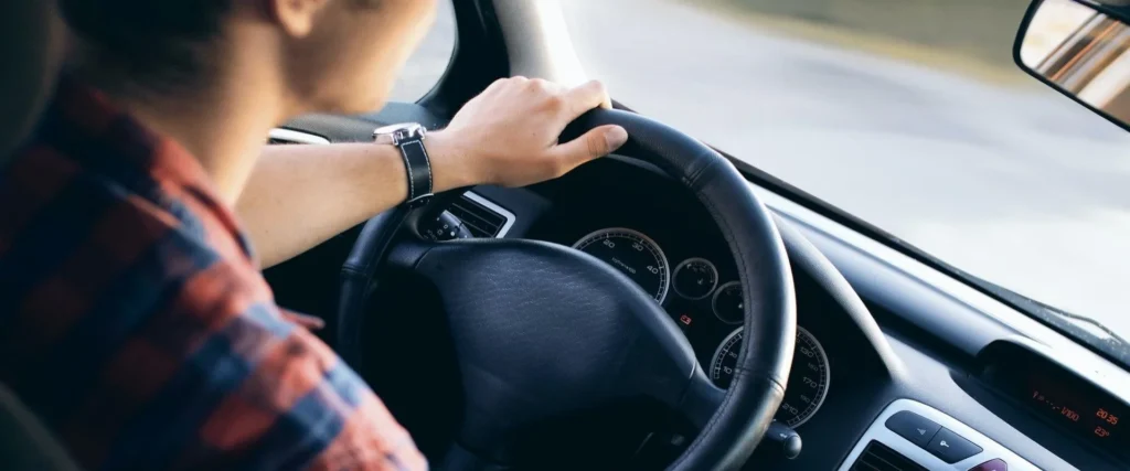 Nell'immagine un uomo seduto in macchina con le mani sul volante.