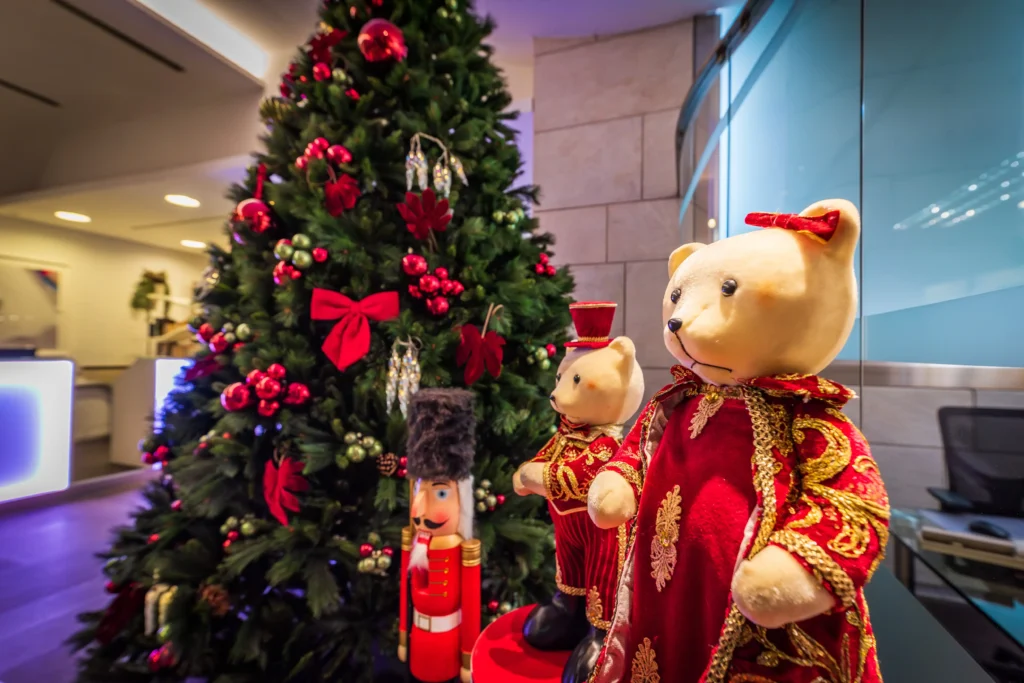 Nell'immagine un albero di Natale addobbato con decorazioni rosse, uno schiaccianoci in legno e due orsacchiotti.