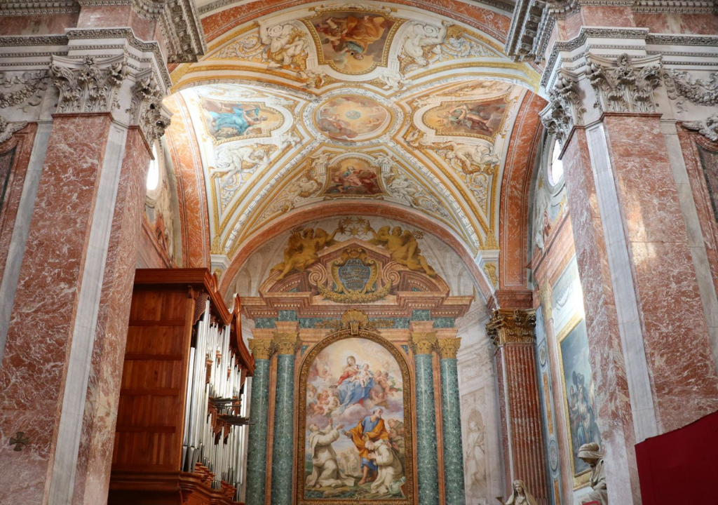 l'immagine rappresenta l'interno della basilica, con volte e colonne in marmo, affreschi e sulla sinistra l'organo.