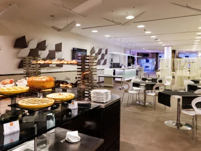 The picture shows part of the breakfast buffet with tarts, croissants and pies for serving. In the same room there are also tables with chairs set up for guests.