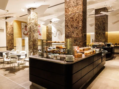 The picture shows in the foreground one of the buffets, set up on an island table, with croissants, cereals and biscuits. In the background are a few small tables with chairs where guests can sit and have breakfast.