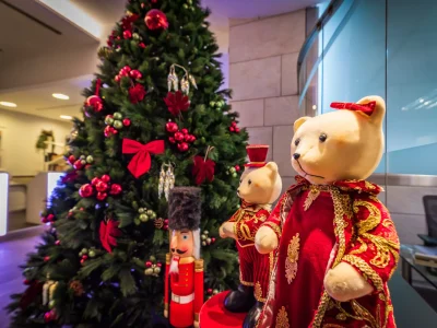 Nell'immagine un albero di Natale addobbato con decorazioni rosse, uno schiaccianoci in legno e due orsacchiotti.