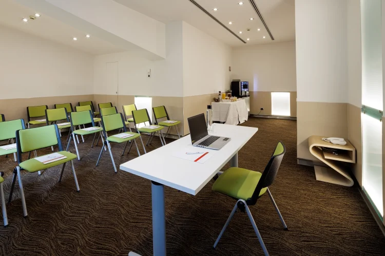 Nella foto, una vista della Sala riunioni Priscilla con la disposizione dei posti a sedere. Davanti c'è un tavolo per gli oratori e a lato uno schermo per le proiezioni. In un angolo si trova anche un piccolo buffet per la pausa caffè.