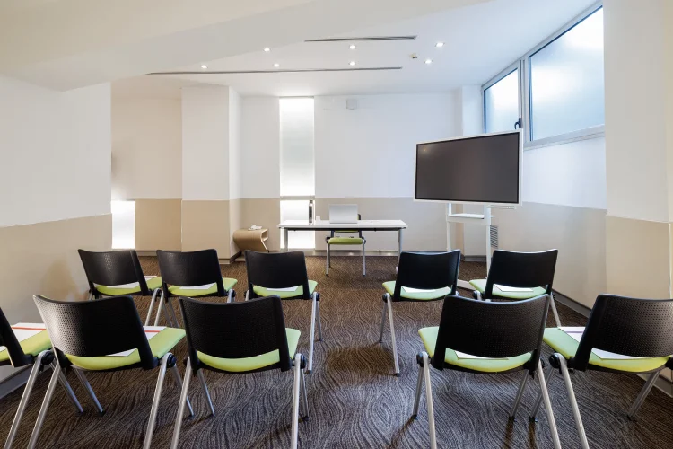 Nella foto, una vista della Sala riunioni Priscilla con la disposizione dei posti a sedere. Davanti c'è un tavolo per i relatori e a lato uno schermo per le proiezioni.