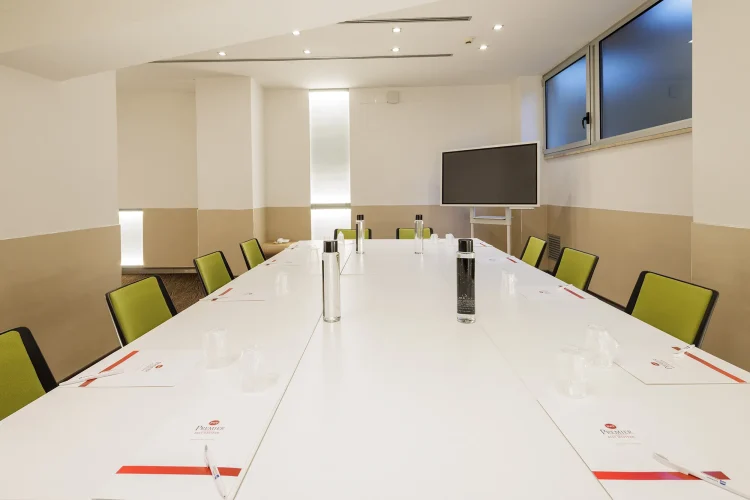 Nella foto, la sala riunioni Priscilla è dotata di un tavolo singolo con dodici posti a sedere. Su un lato c'è anche uno schermo per le proiezioni.