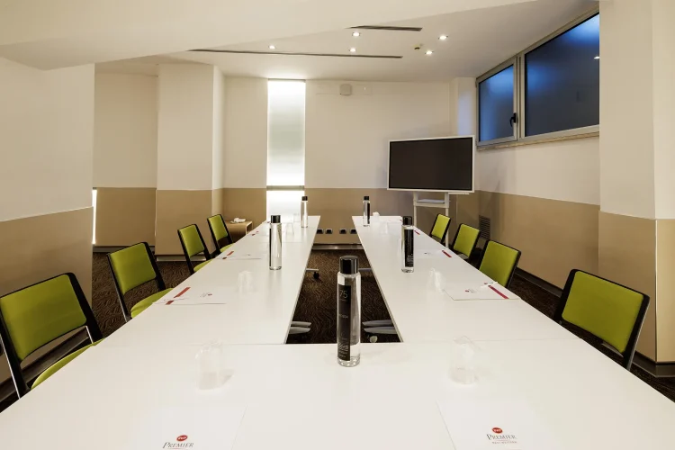 Nella foto, la sala riunioni Priscilla ha una disposizione a ferro di cavallo con dieci postazioni. Su un lato c'è anche uno schermo per le proiezioni.