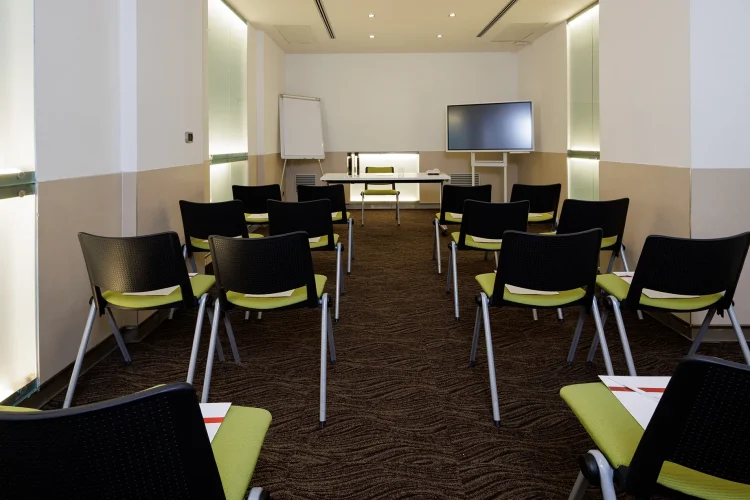 Nella foto, la Sala riunioni Rachel è allestita come un auditorium. Nella sala sono presenti anche uno schermo di proiezione e una lavagna a fogli mobili, oltre a un tavolo per i relatori.