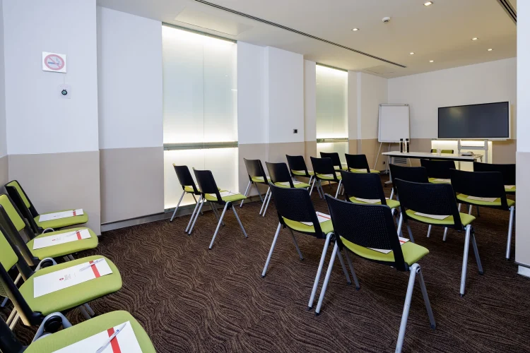 Nella foto, la Sala riunioni Rachel è allestita come un auditorium. Nella sala sono presenti anche uno schermo di proiezione e una lavagna a fogli mobili, oltre a un tavolo per i relatori.