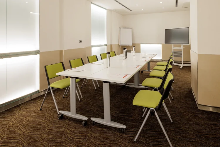 Nella foto, la Sala riunioni Rachel è allestita con un unico tavolo. Nella sala sono presenti anche uno schermo di proiezione e una lavagna a fogli mobili.