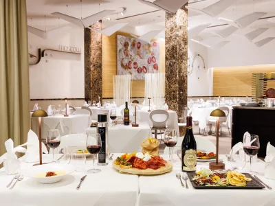 L'immagine del Ristorante The White situato dentro l'Hotel. Si vede un tavolo apparecchiato per quattro persone con alcuni piatti della tradizione e al centro un tagliere di prodotti tipici. Sullo sfondo si vede tutta la sala con i tavoli apparecchiati.