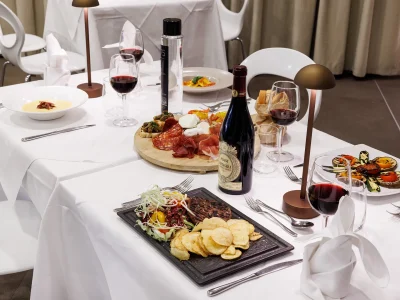 L'immagine del Ristorante The White situato dentro l'Hotel. Si vede un tavolo apparecchiato per quattro persone con alcuni piatti della tradizione e al centro un tagliere di prodotti tipici.